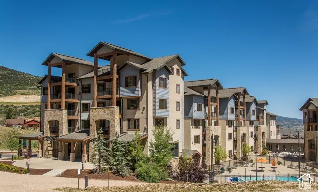 Multi-story building featuring stone and siding exterior, multiple balconies with metal railings, a paved entrance, and a visible outdoor swimming pool