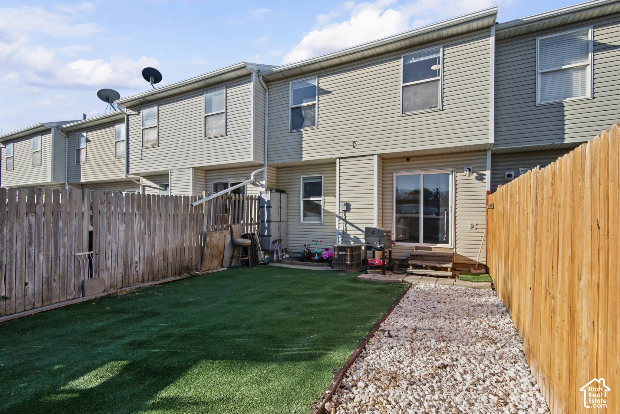 Fenced backyard with artificial turf, gravel pathway, and sliding glass door access