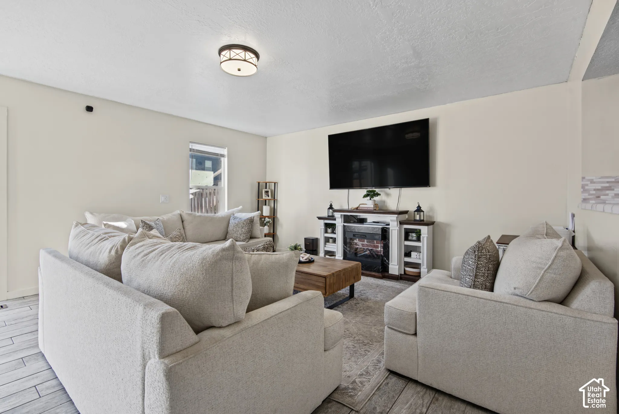 Bright and open living room showcasing neutral upholstered seating, wood-finish flooring throughout, and recessed ceiling lighting