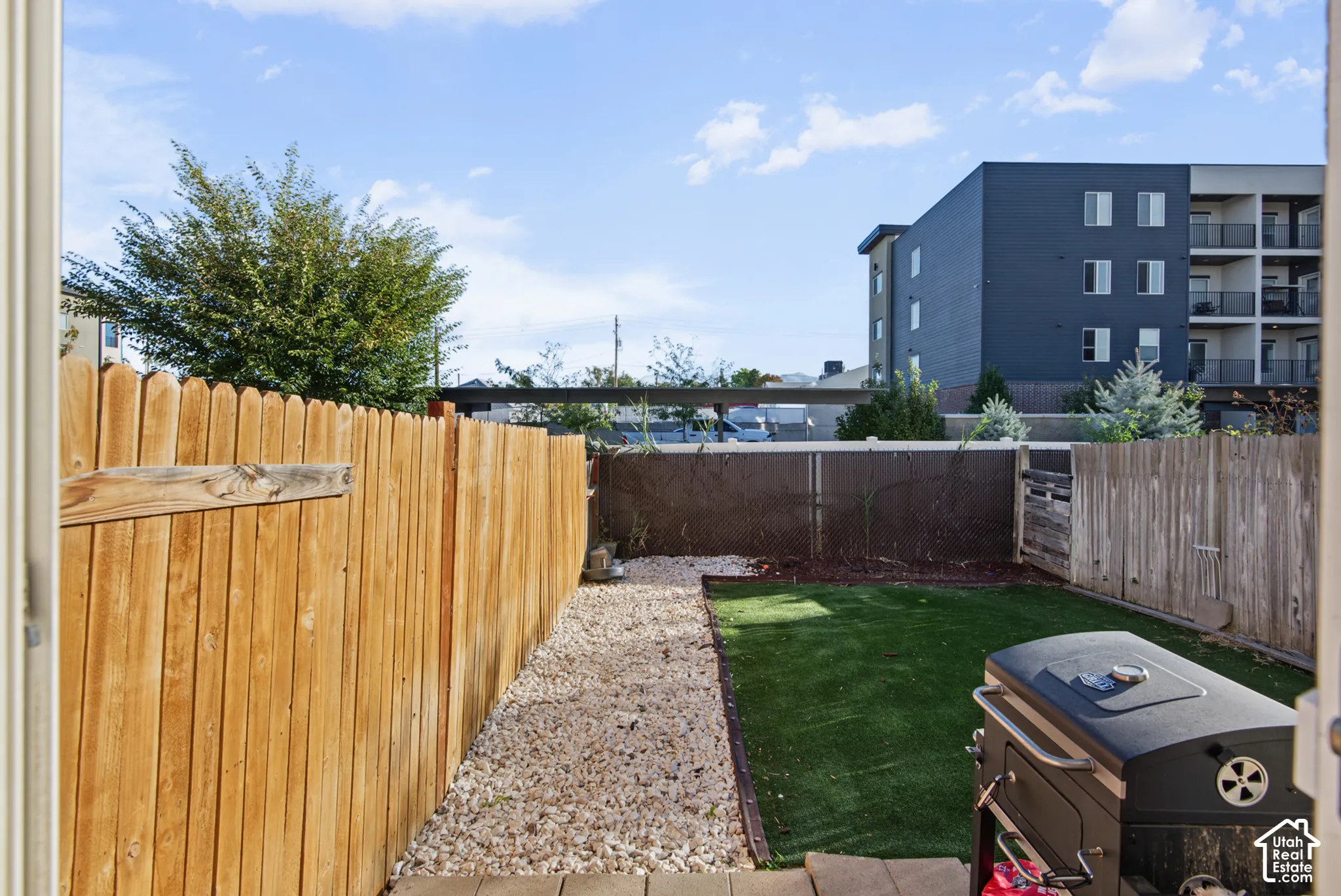 Private outdoor space featuring a wooden privacy fence, gravel pathway, and artificial turf area