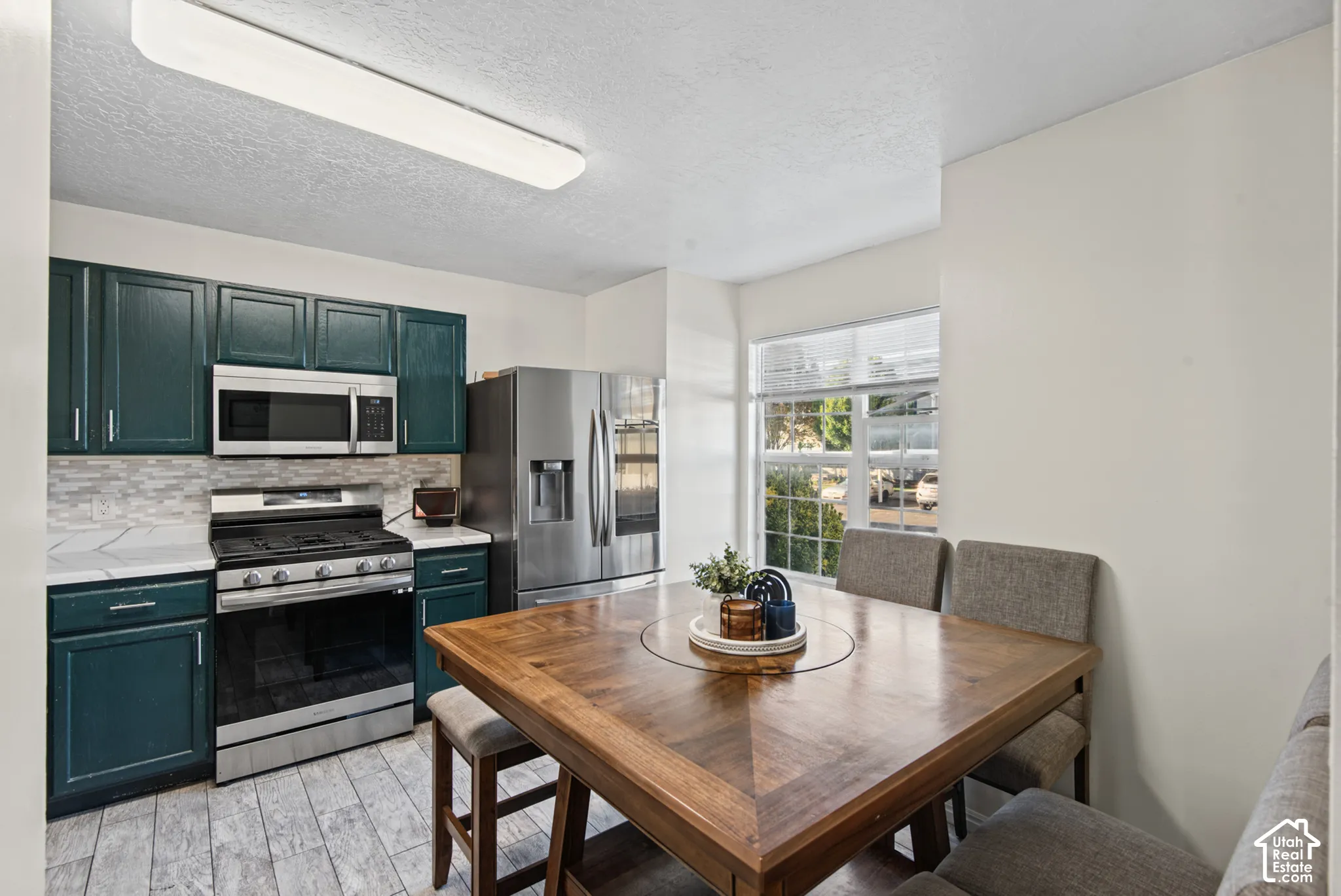 Kitchen featuring stainless steel appliances, dark cabinetry, light-toned countertops, and wood-finish flooring