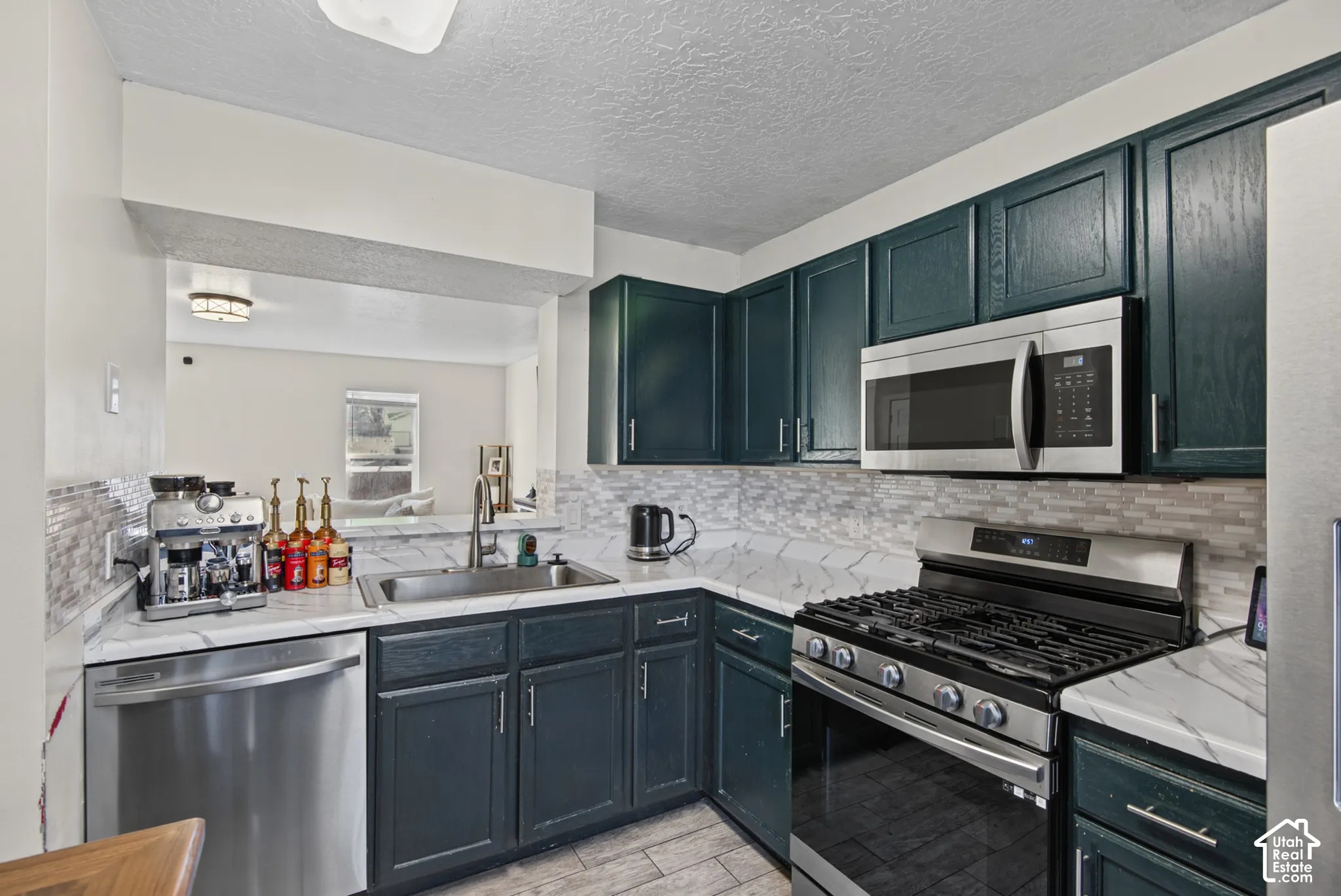 Stainless steel appliances, dark cabinetry, white countertops, tile backsplash, and a stainless steel sink