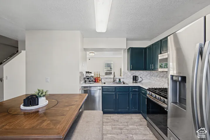 Kitchen with stainless steel appliances, dark blue cabinetry, white marble-look countertops, subway tile backsplash, and wood-finish flooring