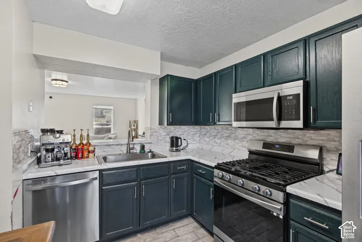 Stainless steel appliances, dark cabinetry, white countertops, tile backsplash, and a stainless steel sink