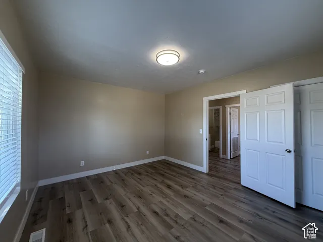 Wood-finish flooring, neutral wall tones, window with blinds, overhead flush-mount lighting, and white paneled doors