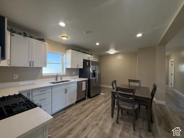 White shaker-style cabinetry with chrome hardware, light-toned countertops, stainless steel appliances, and wood-finish flooring