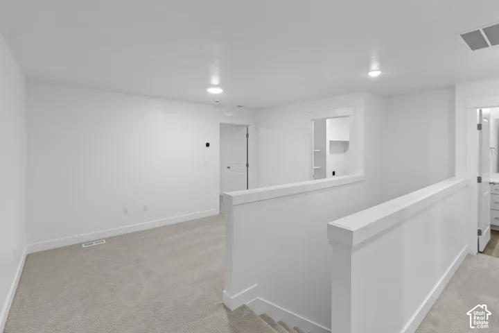 Upper-level landing with neutral carpeting, recessed lighting, white walls, and a white railing system