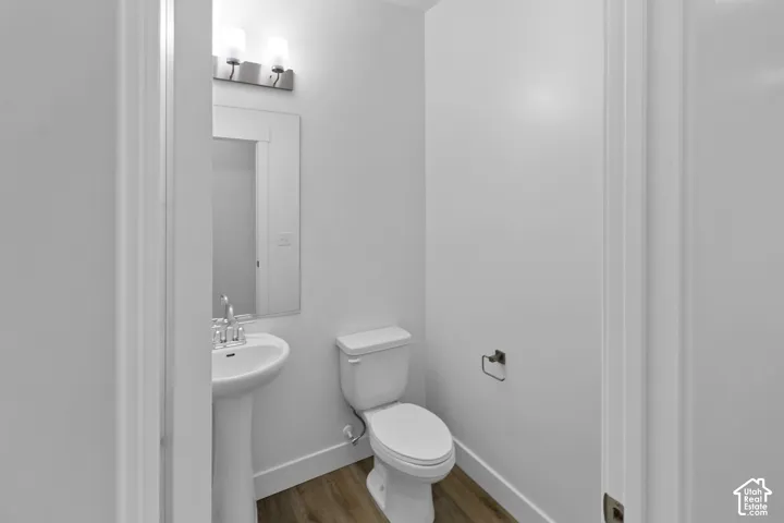 Pedestal sink with chrome faucet, wall-mounted mirror, and wood-finish flooring