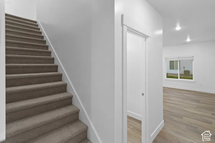 Carpeted staircase, white trim details, recessed lighting, wood-finish flooring, and a large window