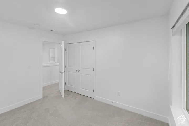 Recessed ceiling light fixture, neutral carpeting, white interior doors, and a window with a roller shade