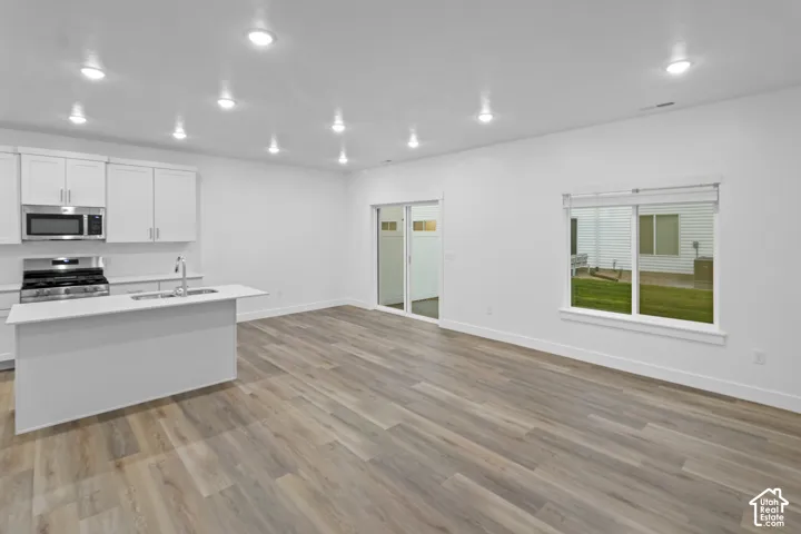 Kitchen with white cabinetry, stainless steel appliances, a center island with sink, wood-finish flooring, and recessed lighting