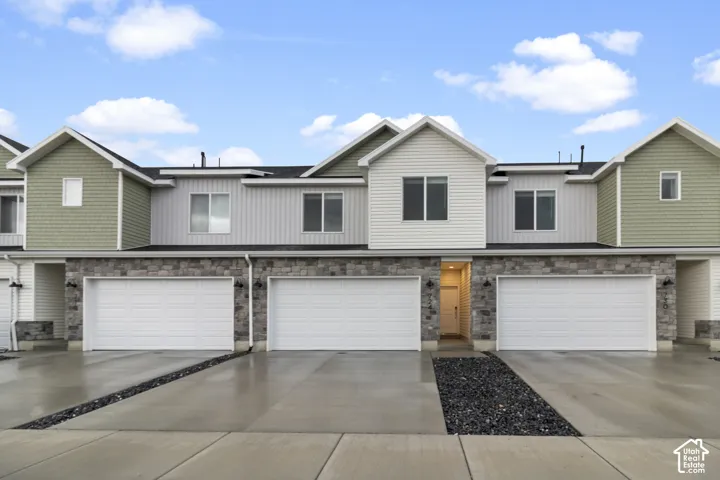 Contemporary multi-unit exterior featuring vertical and horizontal siding, stone facade, multiple garage bays with individual doors, and paved driveway entries