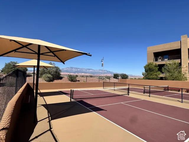 Community tennis/pickleball courts with perimeter fencing, two shade umbrellas, and mountain scenery