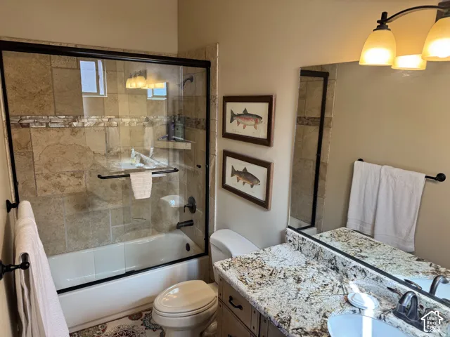 Bathroom featuring a tiled shower/tub combination with a glass enclosure, a vanity with a stone countertop, an integrated sink, and an overhead light fixture