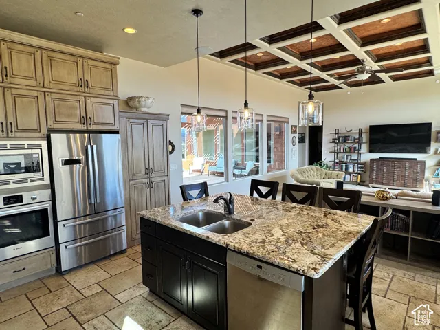 Gourmet kitchen featuring stainless steel appliances, large kitchen island with integrated sink, coffered ceiling, and tile flooring