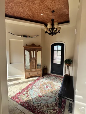 Recessed entryway featuring a coffered ceiling with a textured finish, a dark wood chandelier, and a solid door with decorative glass inserts