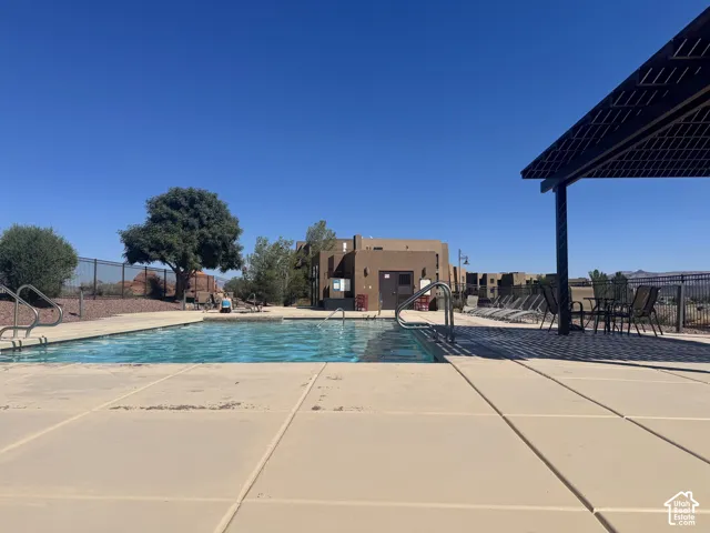Outdoor swimming pool with integrated steps, surrounded by a concrete patio and a shaded pergola area