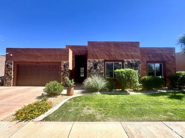 Southwestern style exterior with stucco and stone accents, two-car garage, mature landscaping, and a manicured lawn