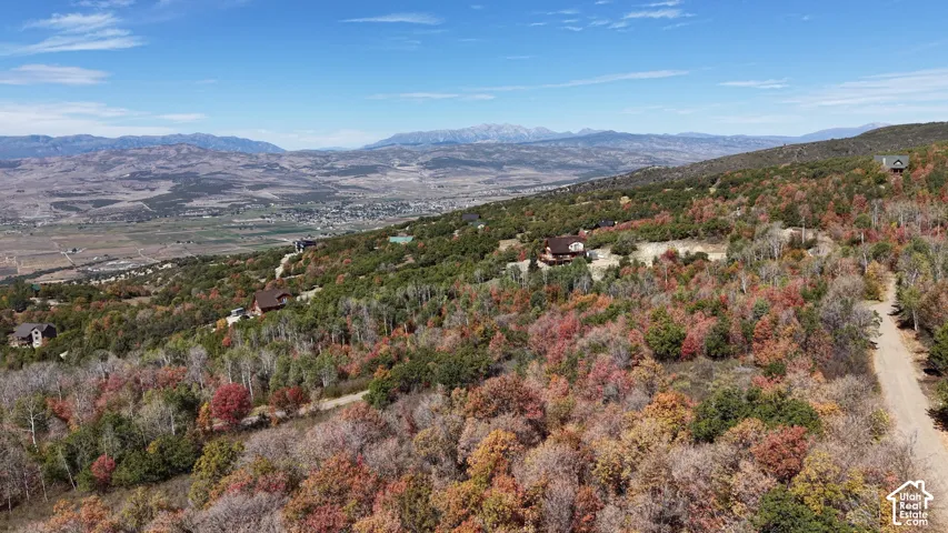 Mountainous terrain with natural vegetation, scattered residential structures, distant valley, and clear skies
