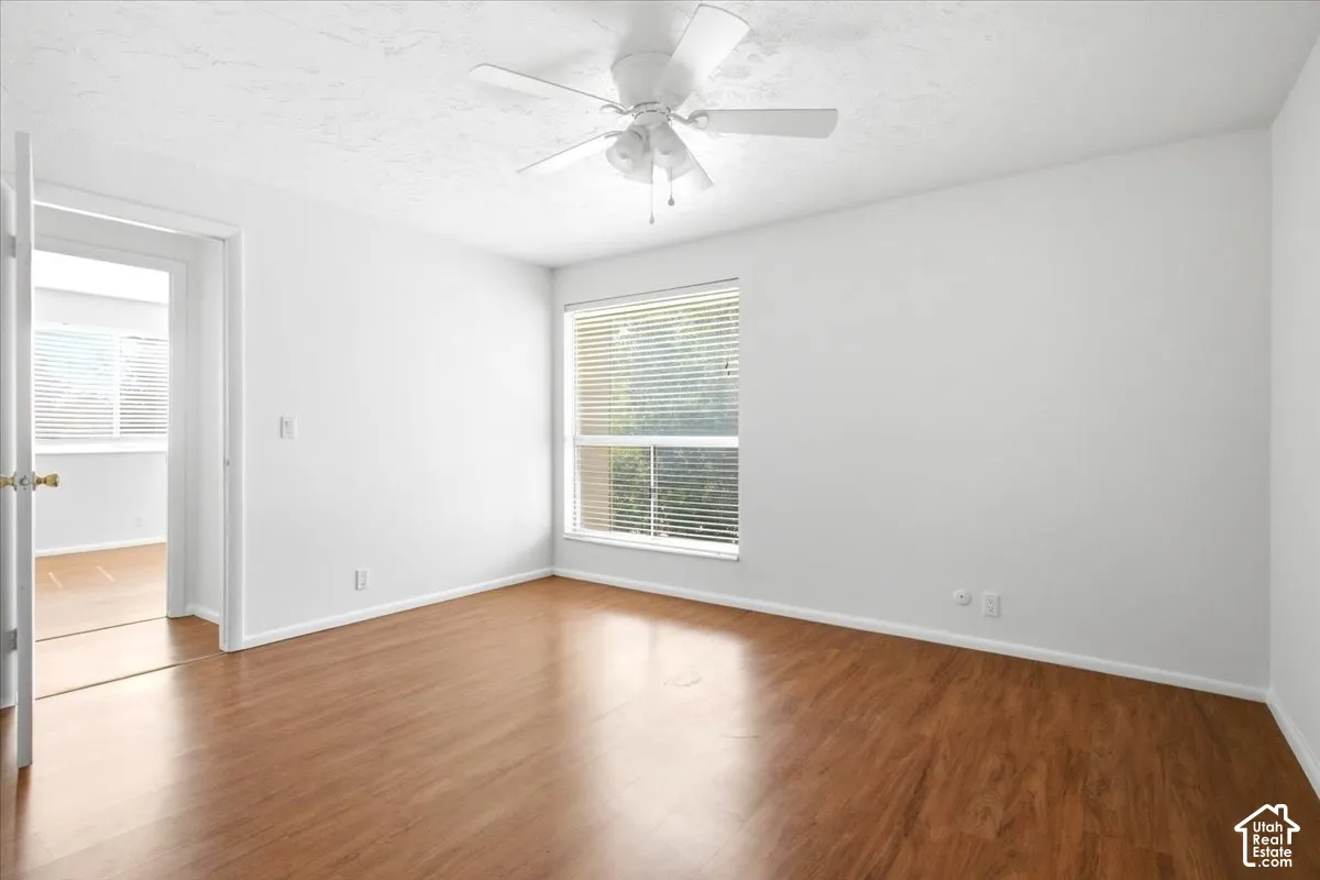 Wood-finish flooring, white walls, ceiling fan, and a window with blinds