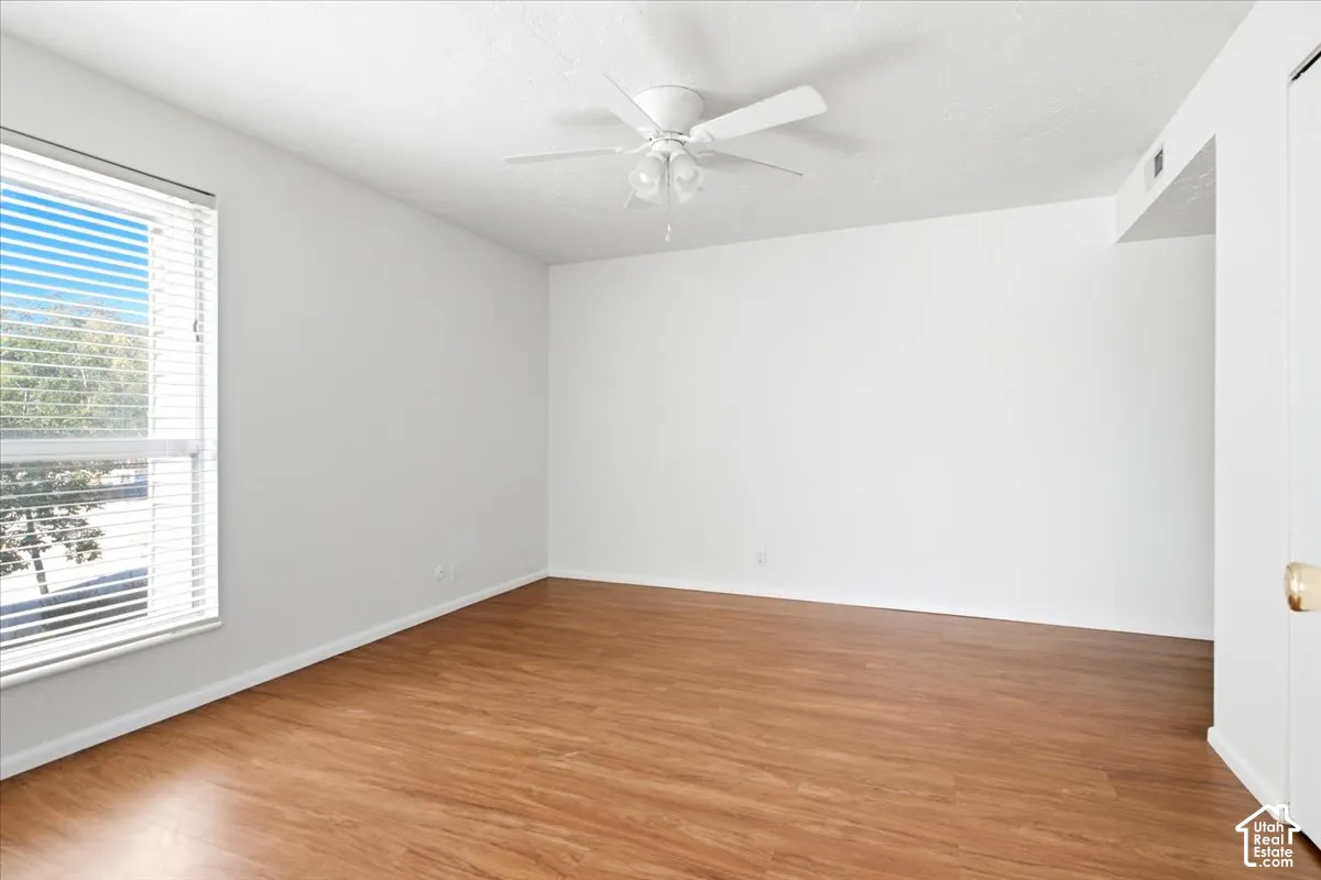 Wood-finish flooring, white walls, ceiling fan with light fixture, and a window with blinds