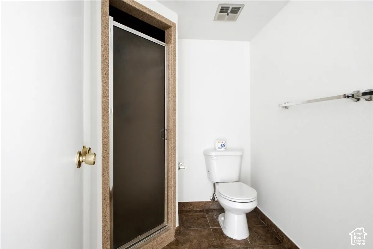Shower enclosure with textured glass panel, brass door hardware, white toilet, and dark tile flooring