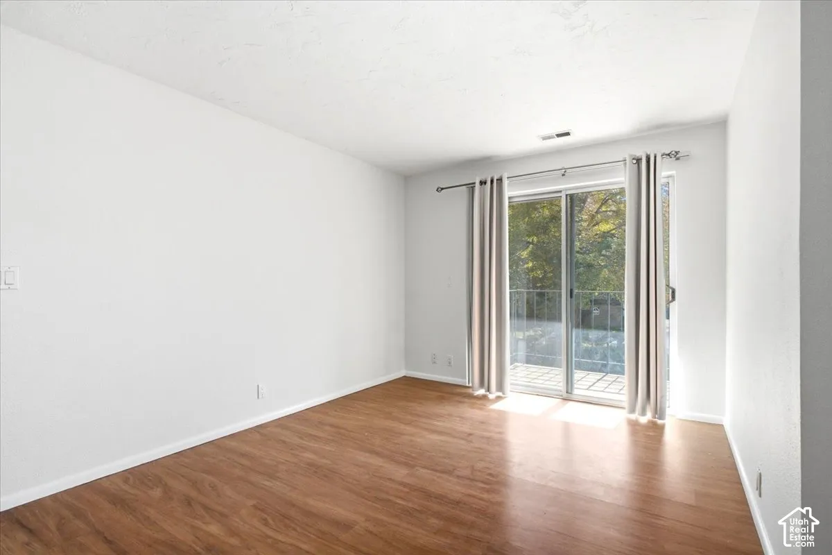 Wood-finish flooring with white baseboards, white walls, and a sliding glass door providing access to an outdoor patio with a metal railing