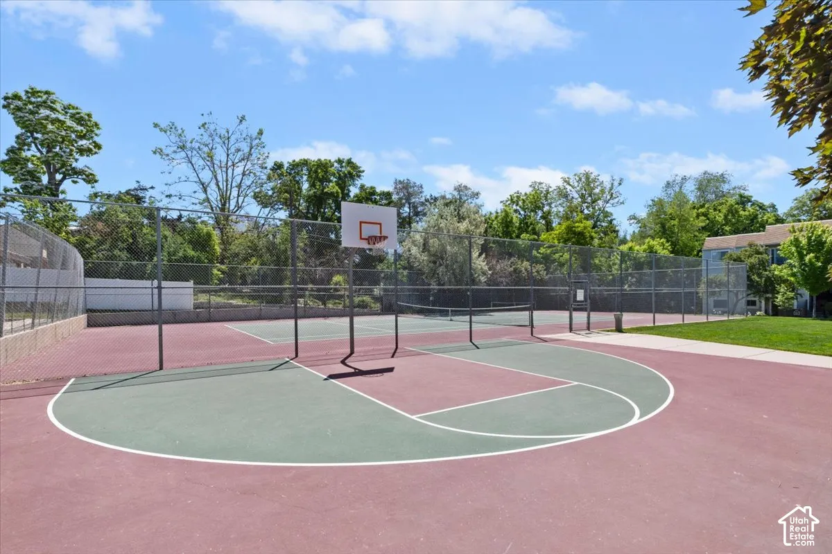 Sport court featuring a basketball hoop, tennis net, and perimeter fencing