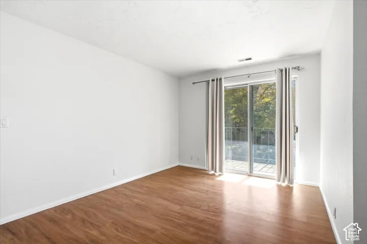 Wood-finish flooring with white baseboards, white walls, and a sliding glass door providing access to an outdoor patio with a metal railing
