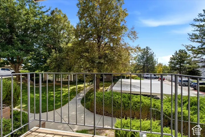 Balcony with metal railing overlooking a manicured lawn, established trees, and a concrete pathway