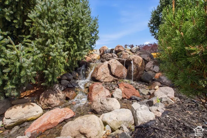 Tiered rock waterfall feature with natural stone accents, surrounded by mature evergreen plantings and dark mulch