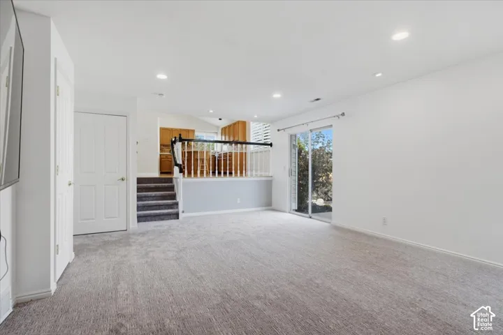Recessed lighting illuminates the carpeted living area, featuring a sliding glass door and a staircase with a wood railing