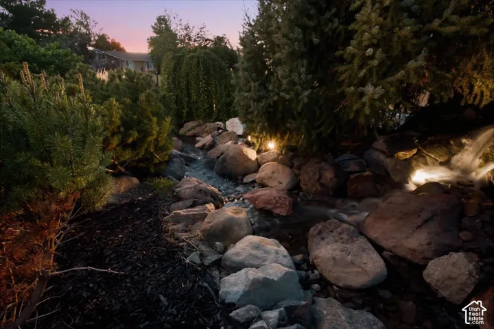 Rock-lined water feature with a waterfall element, surrounded by diverse plantings and uplighting