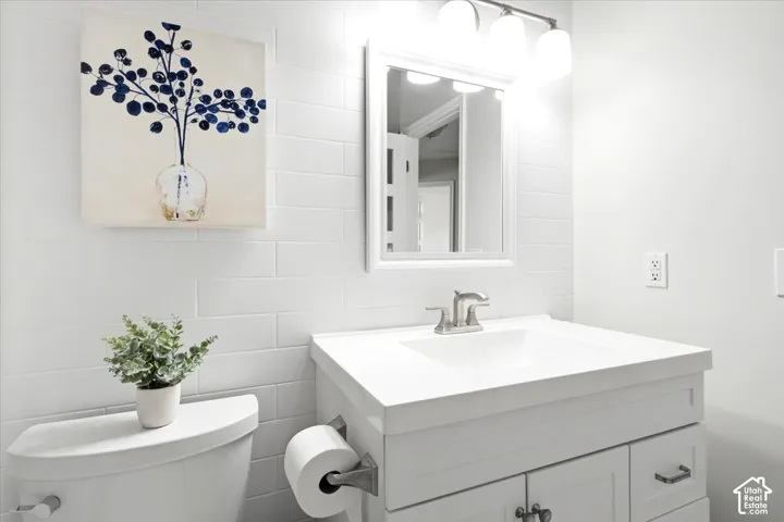 White subway tile backsplash, white vanity with integrated sink, brushed nickel faucet, wall-mounted mirror, and overhead vanity lighting