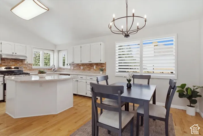 Vaulted ceilings, wood-finish flooring, white cabinetry, integrated kitchen island, and a decorative chandelier
