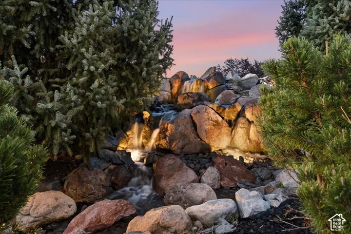 Tiered rock water feature, mature evergreen landscaping, and integrated accent lighting