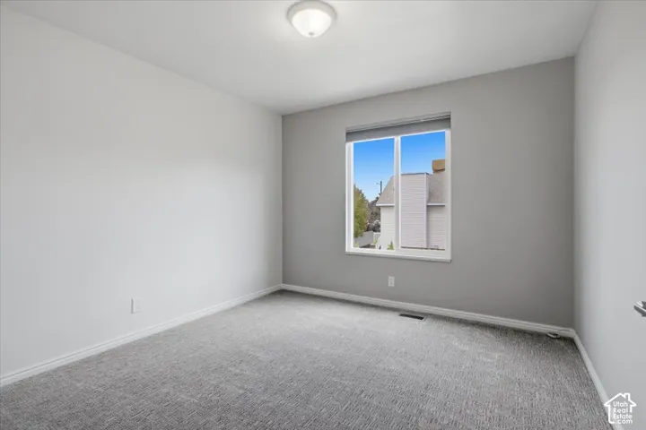 Neutral gray wall paint, gray patterned carpet, white trim, recessed lighting, and a single window with roller shade