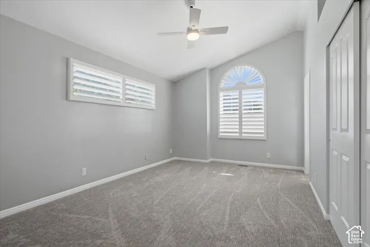 Vaulted ceiling with a ceiling fan and light fixture, arch-top window with plantation shutters, additional windows with plantation shutters, and light gray wall paint