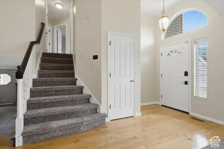 Entryway featuring wood-finish flooring, a white paneled door with an arched transom, a large arched window, and a carpeted staircase with white risers and a dark wood handrail