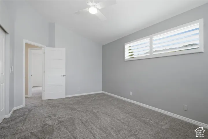 Vaulted ceiling with a ceiling fan, gray carpet flooring, rectangular window with plantation shutters, and a five-panel interior door
