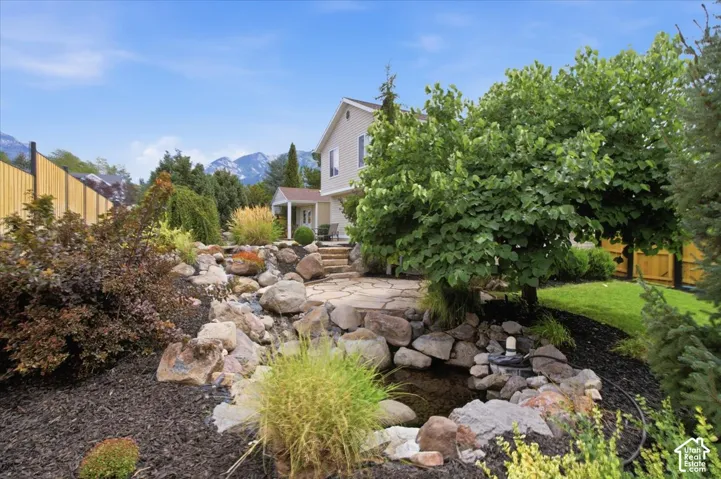 Expansive backyard featuring a rock water feature, flagstone patio, mature tree, and diverse landscaping