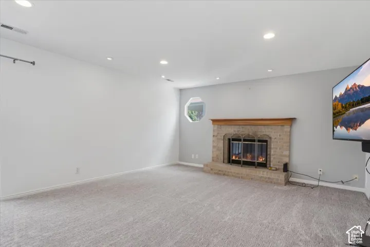 Recessed lighting illuminates the carpeted floor and brick fireplace with a wood mantel