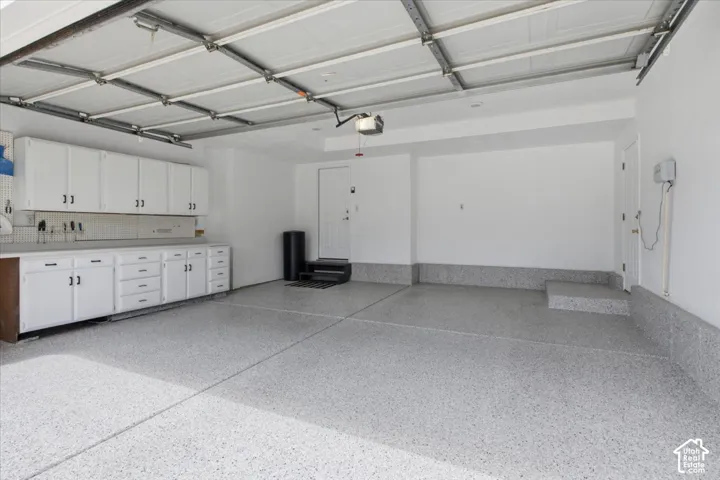 Spacious garage featuring a durable speckled epoxy floor finish, extensive white cabinetry with dark hardware, and a bright white overhead garage door