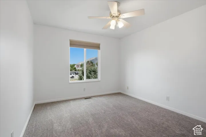 Recessed window with roller shade, overhead ceiling fan with light fixture, light gray carpeting, and white wall paint