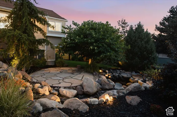 Flagstone patio with an integrated water feature, surrounded by natural rock formations and mature landscaping with accent lighting