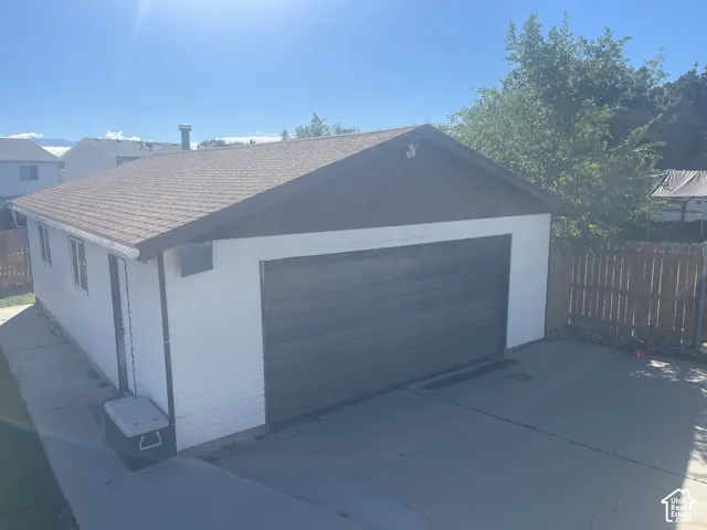 Detached garage with a brown asphalt shingle roof, white siding, and a dark brown garage door