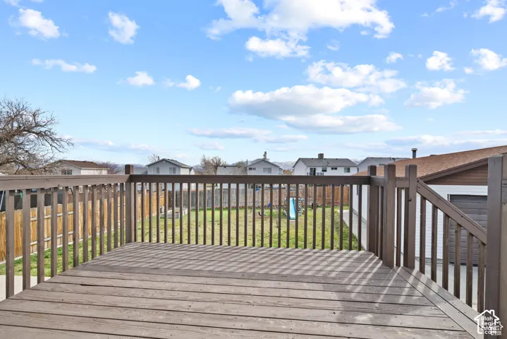 Wood-finish deck with a full railing and balusters, overlooking a fenced yard and surrounding properties