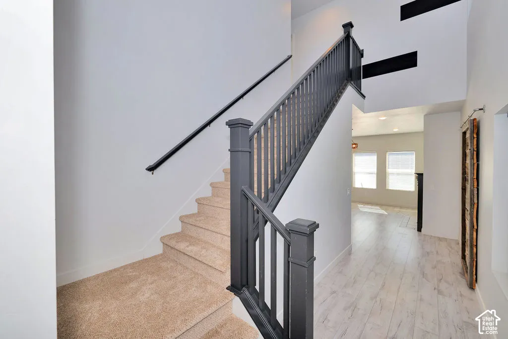 Entryway featuring a double-height ceiling, wood-finish flooring, and a staircase with a dark-painted wooden railing and carpeted treads
