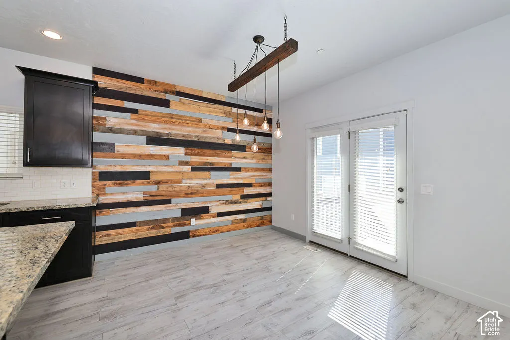 Accent wall featuring multi-toned horizontal wood planking, wood-finish flooring, dark-toned cabinetry, light-colored stone-patterned countertops, and a suspended multi-light fixture with a timber beam element