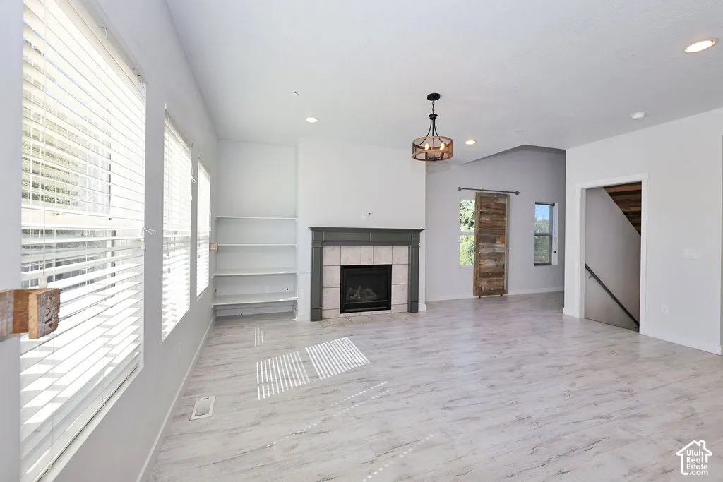 Fireplace featuring a stone tile surround and dark wood mantel, built-in shelving, wood-finish flooring, recessed lighting, and a sliding wood-finish barn door